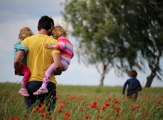 Vater trägt seine Kinder über eine Blumenwiese